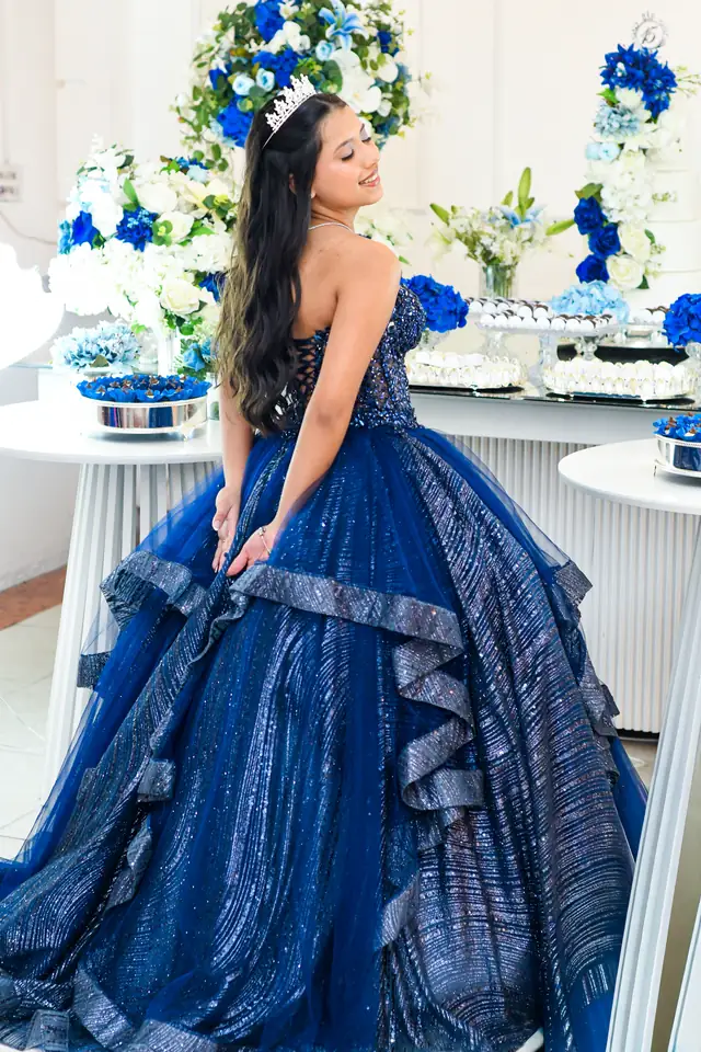 Debutante de vestido azul-marinho, de costas, diante de uma mesa de doces azul e branca