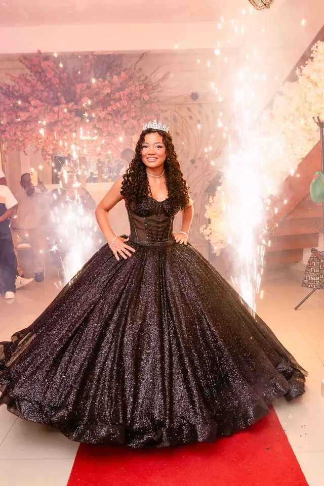 Debutante de vestido preto cintilante sobre tapete vermelho, com faíscas de efeito ao fundo