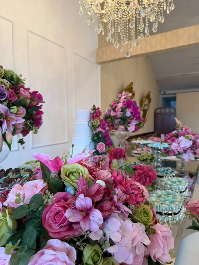 Mesa de doces rosa com flores sob lustre de cristal no Buffet Melvalen