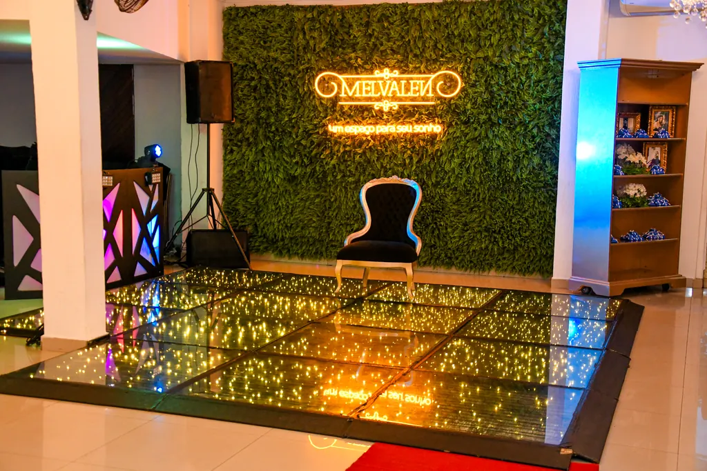 Pista com piso de LED, trono preto e dourado e parede verde com o neon do Buffet Melvalen, cenário da festa de 15 anos