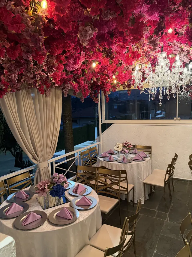 Dois lustres de cristal sob um teto de flores vermelhas, na varanda do Buffet Melvalen com mesas postas